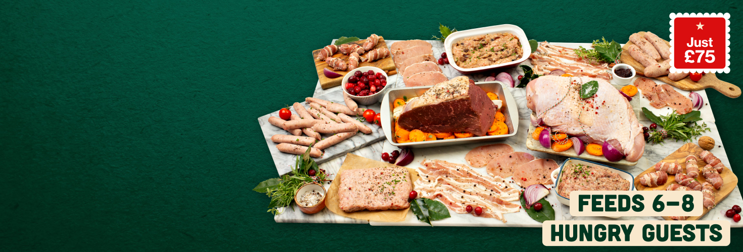 A large variety of festive raw meats arranged on marble boards with a beef topside joint and a turkey butterfly at the centre